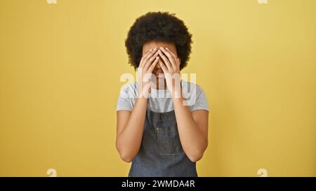 Porträt einer emotionalen afrikanerin, die ihre Augen mit ihren Händen vor gelbem Hintergrund bedeckt Stockfoto