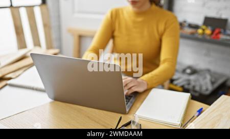 Fokussierte Frau, die in einer Holzwerkstatt am Laptop arbeitet. Stockfoto