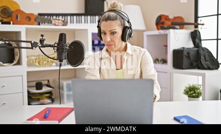 Junge blonde Reporterin, die einen Laptop benutzt, der in Radiosendungen im Radio-Studio spricht Stockfoto