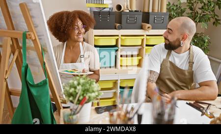 Selbstbewusste Künstler, zwei lächelnde Partner, die sich im Herzen ihres Ateliers zusammenschließen Stockfoto
