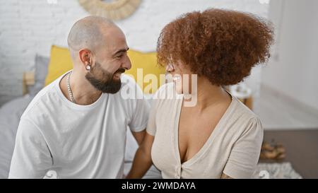 Ein nettes, selbstbewusstes Paar genießt einen lustigen Morgen zusammen, sitzt auf ihrem Bett, wacht mit Lächeln und Freude auf und sieht sich gegenseitig in ihrem wunderschönen Bett an Stockfoto