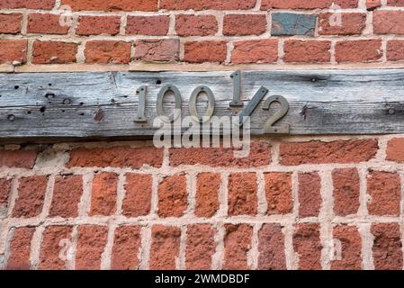 Altes und verwittertes hölzernes Adressschild mit Metallziffern, ungewöhnliche Nummer 100 1/2. Stockfoto