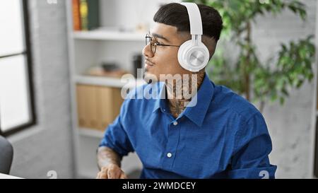 Seriöser und stilvoller junger latin-Mann, der die Show im Büro leitet, Kopfhörer an, in Gedanken verloren, im Takt schwingt, während er die Geschäftswelt beherrscht Stockfoto