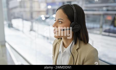 Eine junge Frau, die ein Headset trägt, steht vor einem verschwommenen Hintergrund und strahlt Professionalität aus. Stockfoto