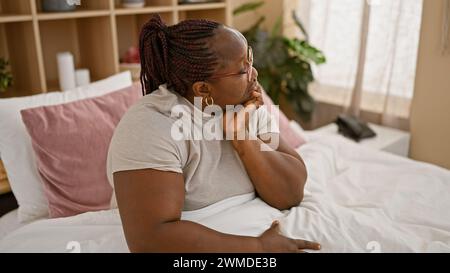 Übergroße afroamerikanische Frau mit Zöpfen, die von Stress überwältigt aussieht, rastlos auf ihrem Bett ruht, erschöpft und besorgt, mit mir zu kämpfen Stockfoto