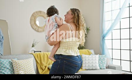 Glückliche Mutter steht zuversichtlich zu Hause, hält ihre liebenswerte Tochter in den Armen und genießt gemeinsam die Liebe der Familie in ihrem Wohnzimmer mit einem Stockfoto