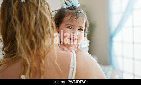Glückliche Mutter steht zuversichtlich zu Hause, hält ihre liebenswerte Tochter in den Armen und genießt gemeinsam die Liebe der Familie in ihrem Wohnzimmer mit einem Stockfoto
