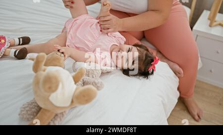 Mutter und Tochter sind verbunden, kichern viel vom Kitzeln, während sie im gemütlichen Schlafzimmer auf dem Bett sitzen Stockfoto