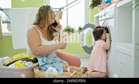 Mutter und Tochter, die sich über Hausarbeiten unterhalten, ein herzerwärmendes Gespräch auf einem Smartphone in der Wäscherei, während sie ihre Familie waschen Stockfoto