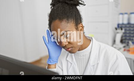 afroamerikanische Wissenschaftlerin im Labor mit Handschuhen, die Daten auf dem Computerbildschirm analysiert Stockfoto