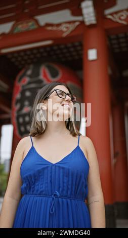 Fröhliche, wunderschöne hispanische Frau mit Brille, die freudig den majestätischen Senso-JI-Tempel erkundet und bewundert, während sie lässig schlendert und sich umsieht Stockfoto