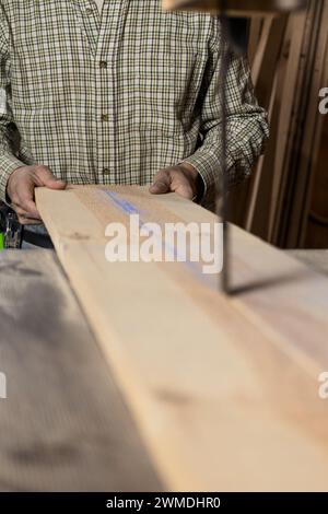 Vertikale Fotohände eines Zimmermannes mittlerer Erwachsener kaukasier richten eine Holzdiele sorgfältig auf ein Bandsägeblatt aus, wobei der Fokus auf der markierten Richtlinie für liegt Stockfoto