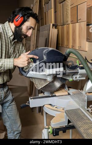 Vertikales Foto Ein fokussierter Zimmermann schneidet eine Holzdiele mit einer Gehrungssäge und achtet dabei auf einen präzisen Winkelschnitt. Geschäftskonzept. Stockfoto