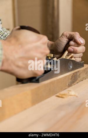 Vertikales Foto eine Nahaufnahme, bei der die Hände eines fokussierten Zimmermanns erfasst werden, während sie einen Holzbalken abheben und zarte Schnitte erzeugen. Kopierbereich. Geschäftsleute Stockfoto