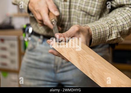 Horizontaler fotofokussierter Handwerker, der mit einem Meißel ein Stück Holz von Hand schnitzt und dabei das Können der traditionellen Holzbearbeitung unter Beweis stellt. Business Co Stockfoto