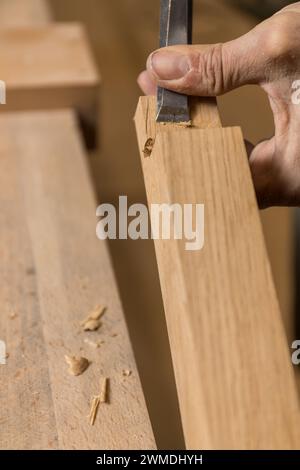 Vertikale, fotofokussierte Handwerkskunst, während ein Zimmermann mit einem scharfen Meißel und stabilen Händen eine präzise Kerbe in ein Stück Holz schneidet. Kopieren Stockfoto