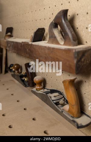 Vertikales Foto eine Sammlung klassischer hölzerner Handflugzeuge liegt auf einem Regal, mit einem Hintergrund aus Pinnwänden, der auf den Raum eines traditionellen Holzarbeiters hinweist. Stockfoto