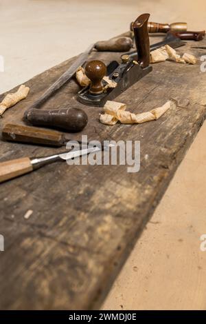 Fotografieren Sie eine Reihe von Holzschnitzereien, darunter Meißel und ein Handflugzeug, liegen Sie auf einer verwitterten Werkbank mit verstreuten Holzspänen, die an einen erinnern Stockfoto