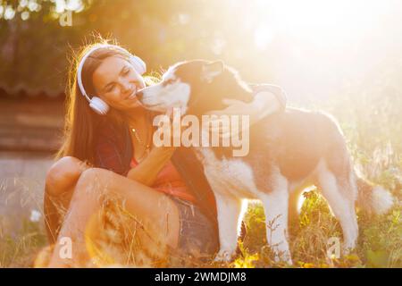 Frau genießt Musik mit ihrem Husky im Sonnenlicht Stockfoto
