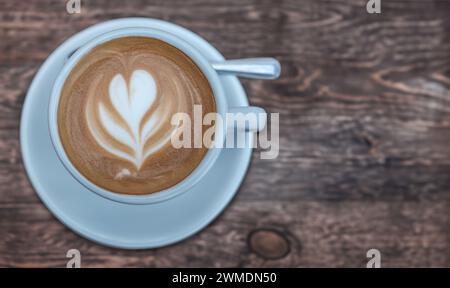 Eine Tasse Kaffee, komplett mit Latte Art in der aufschäumenden Milch, auf Einem rustikalen Kaffeetisch mit Kopierraum Stockfoto