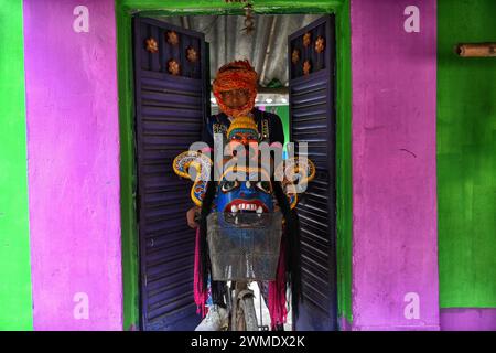 Kushmandi, Indien. Februar 2024. Eine maskierte Tänzerin der Gomira-Tanztruppe, die eine Maske auf dem Fahrrad trägt. Gomira ist eine maskierte Tanzform. Das Wort ''˜Gomira' stammt von der umgangssprachlichen Form des Wortes ''˜Gram-Chandi' oder der weiblichen Gottheit, die die Schutzkraft des Dorfes ist. Der genaue Ursprung der Tanzform ist nicht nachvollziehbar und das Wissen ist im Laufe der Zeit verloren gegangen. Der Gomira-Tanz ist eine ländliche Tanzform, die hauptsächlich im Distrikt Dinajpur in Westbengalen praktiziert wird. Die Gomira-Tänze werden organisiert, um die Gottheit zu besänftigen, die „Guten Mächte“ einzulassen und die „bösen Mächte“ zu vertreiben. Stockfoto