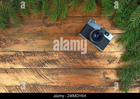 Die alte Kamera auf hölzernem Hintergrund und Zweige von Weihnachtsbaum. Weihnachtshintergrund. Nostalgie. Erinnerungen. Vergangenheit. Neujahr. Draufsicht. Nahaufnahme. Stockfoto