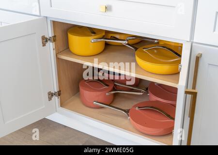 Buntes Kochgeschirr mit Töpfen, Pfannen und Töpfen in weißem Küchenschrank Stockfoto