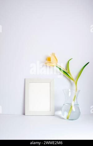 Leerer Bilderrahmen und gelbe Tulpe in Vase auf weißem Hintergrund. Feiertags-, Frauentag- oder Muttertagskonzept. Stockfoto