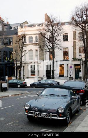 Ein geparkter Oldtimer vor einer Reihe von Häusern in Notting Hill, London. Dieses beliebte Viertel ist bekannt für seine farbenfrohen Häuser und Architektur. Stockfoto