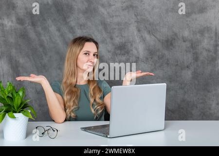 Junge Frau mit blondem Haar und grauem Kleid in verschiedenen Posen mit Laptop und grüner Blume Stockfoto