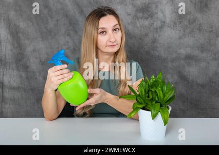 Junge Frau mit blondem Haar, die grüne Topfpflanzen drinnen tränkt Stockfoto
