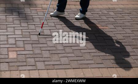 Eine gesichtslose blinde Frau läuft mit einem Stock die Straße entlang. Stockfoto