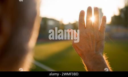 Alter Mann Großvater Rentner Blick Sonnenaufgang Sonne durch Palmenhand Morgen Nahaufnahme nicht erkennbare männliche Stadion Stadt außerhalb der körperlichen Aktivität Stockfoto