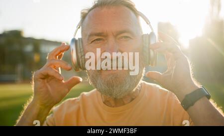 Kaukasischer Europäischer Rentner bei Sonnenaufgang Kopfhörer aufsetzen Musik hören Entspannung morgens Workout Sport körperliche Bewegung Stadion im Freien Stockfoto