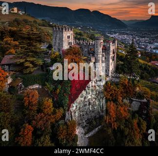 Merano, Italien - Panoramablick aus der Vogelperspektive auf das berühmte Schloss Brunnenburg (Castel Tirolo) mit der Stadt Merano, den italienischen Dolomiten und der bunten Sonne Stockfoto