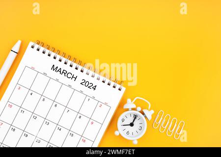 März 2024, monatlicher Schreibtischkalender für 2024 Jahre und Wecker mit Büroklammern auf gelbem Hintergrund. Position mit Kopierraum. Stockfoto