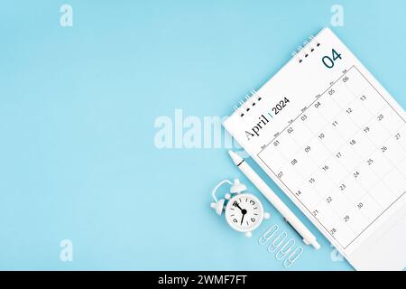 April 2024, monatlicher Schreibtischkalender für 2024 Jahre und Wecker mit Büroklammern auf blauem Hintergrund. Position mit Kopierraum. Stockfoto