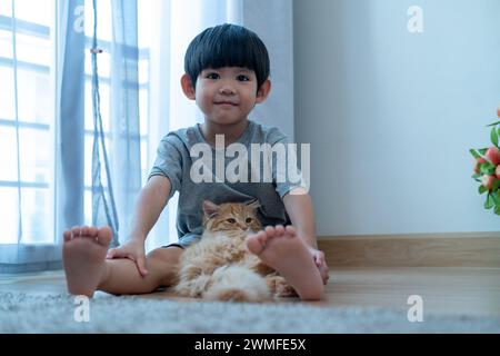 Ein kleiner asiatischer Junge hält liebevoll ein orangenes Kätzchen. Stockfoto