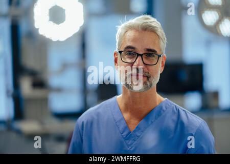 Porträt eines selbstbewussten Notärzten, der in der Notaufnahme des Krankenhauses steht. Ein hübscher Arzt in blauem Gewächs, der in einer modernen Privatklinik stand und ansah, kam Stockfoto