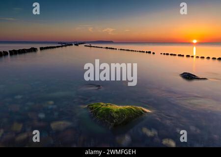 Sonnenuntergang auf der Doppelbühne in Dranske auf der Insel Rügen. Ein grüner, mit Algen bewachsener Stein ist ein schöner Hingucker Stockfoto