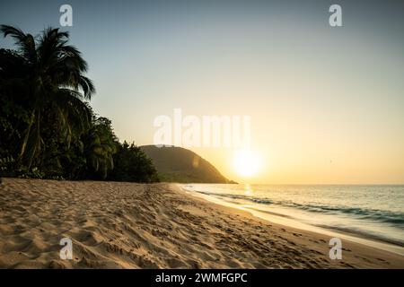 Blick über einen Strand, die Küste und das Meer bei Sonnenuntergang. Im Vordergrund der leere Sandstrand Grande Anse, Basse Terre, Guadeloupe, Französische Antillen Stockfoto