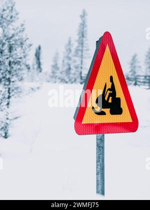 Ein Warnschild in Gelb und Rot befindet sich an der Seite einer schneebedeckten Straße, das auf eine Überquerung des Schneemobils in Schweden hinweist. Stockfoto