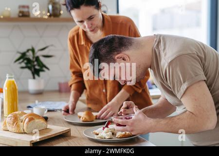 Junger Mann mit Down-Syndrom, der das Frühstück mit seiner Mutter zuhause zubereitet. Morgenroutine für Mann mit Down-Syndrom. Stockfoto