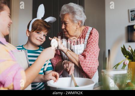 Großmutter mit Enkelkindern backt Kuchen und Süßigkeiten für ostern und hat Spaß. Junge mit Kuchenteig auf der Nase. Familienrezepte weitergeben, Brauch und Stockfoto