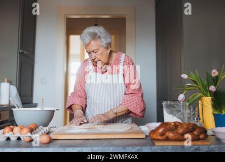 Seniorin, die traditionelle ostermahlzeiten für die Familie zubereitet, Teig für osterbrötchen kneten. Nachbildung von Familienrezepten, individuell. Stockfoto