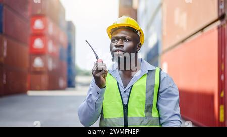 Ein Hafenvorarbeiter mit einem Funkgerät, der vor Frachtcontainern steht Stockfoto