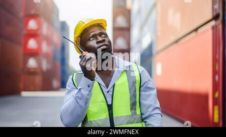 Ein Hafenvorarbeiter mit einem Funkgerät, der vor Frachtcontainern steht Stockfoto