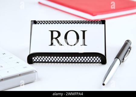 ROI-Konzept. Klicken Sie auf das Wort auf der Visitenkarte, die auf einem Ständer neben einem Notizblock, einem Taschenrechner und einem Stift steht Stockfoto