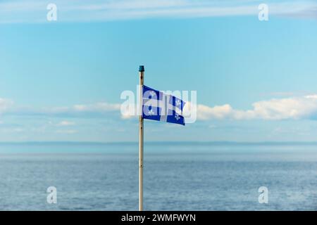 Die Flagge der kanadischen Provinz Québec in der Bildmitte auf einem vertikalen Fahnenmast bewegt sich im Wind im Hintergrund kann man die se sehen Stockfoto
