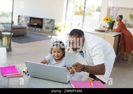 Der birassische Großvater hilft einer jungen Enkelin mit einem Laptop bei der Schularbeit zu Hause Stockfoto